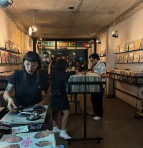 People browsing and playing vinyl records in a dimly lit record store with shelves of albums lining the walls.